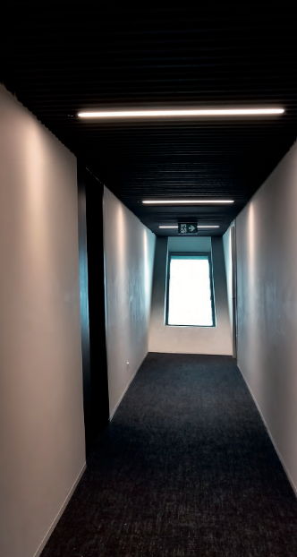 Langer, schmaler Flur mit Beleuchtung und Fenster am Ende.
